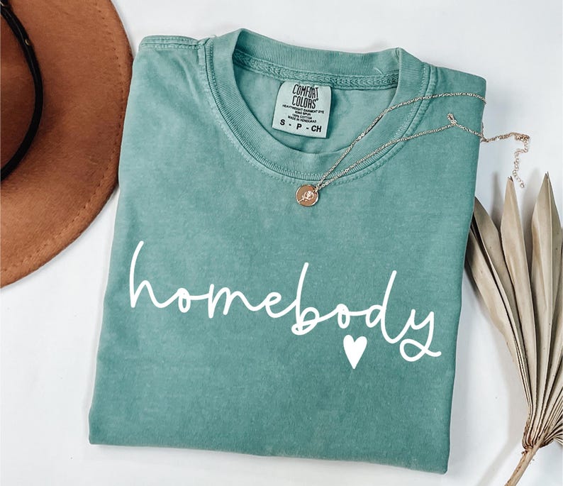 May include: A teal green t-shirt with the text "homebody" in white with a small white heart.