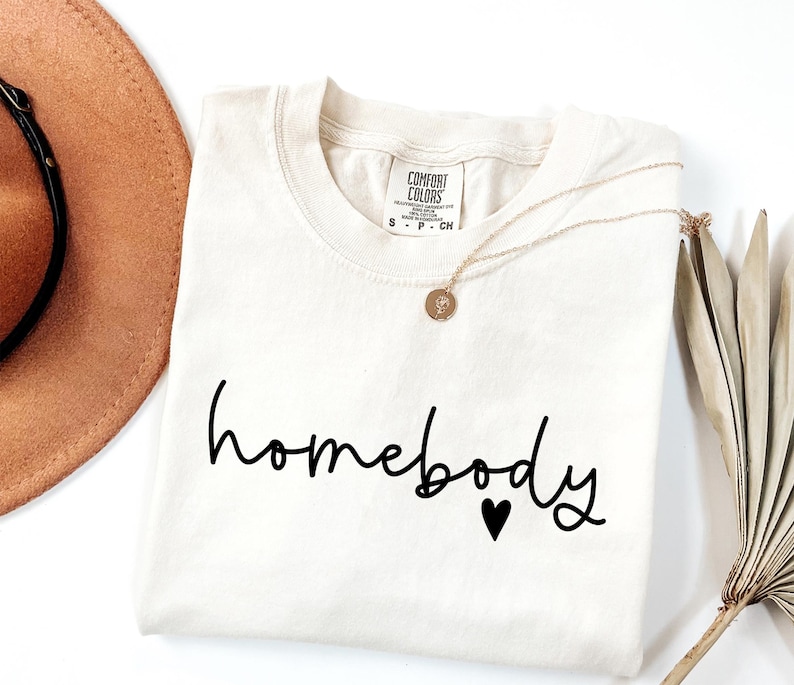 May include: A white t-shirt with the text "homebody" in black script with a small black heart below the text.
