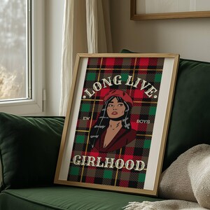 May include: A framed art print featuring a pop art style illustration of a woman wearing a red beret and jacket, set against a plaid background in red, green, and brown. The text "LONG LIVE GIRLHOOD" is displayed.