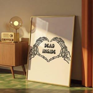 May include: A framed print with a gold border features a heart shape formed by two skeleton hands. The words "DEAD INSIDE" are in the center of the heart. The artwork is on a cream-colored background.