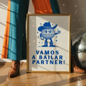 May include: A framed poster with a gold border features a blue cartoon globe character wearing a cowboy hat and boots, giving a thumbs up. The text "VAMOS A BAILAR PARTNER!" is below the character. The poster is displayed against a neutral background.