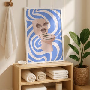 以下が含まれることがあります： 青と白の渦巻き模様を背景に、目と口のある奇抜なトイレのデザインが描かれた額入りのアートプリント。バスルームに飾られており、丸められたタオルと鉢植えの植物が置かれています。