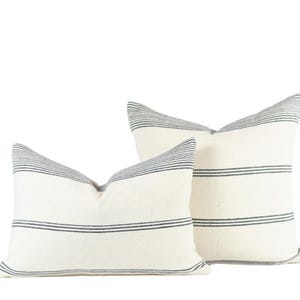 May include: Two white throw pillows with black stripes. The pillows are made of a soft, textured fabric and are perfect for adding a touch of style to any room.