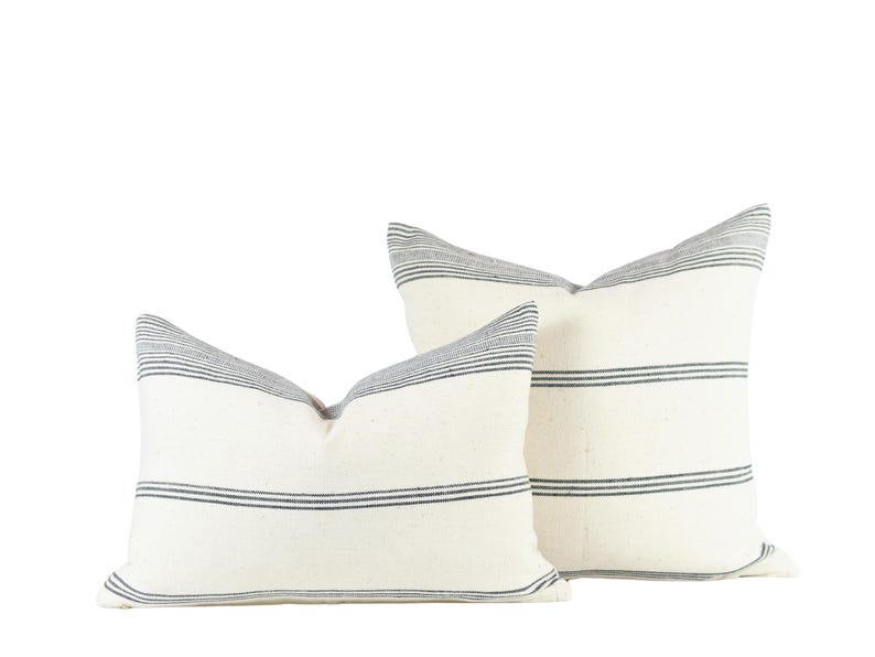 May include: Two white throw pillows with black stripes. The pillows are made of a soft, textured fabric and are perfect for adding a touch of style to any room.