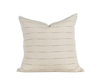 May include: A cream-colored throw pillow with a subtle horizontal stripe pattern in a light brown color. The pillow is made of a soft, textured fabric.