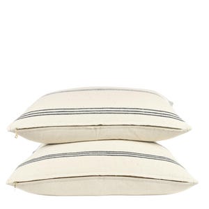 May include: Two white throw pillows with black stripes. The pillows are stacked on top of each other.