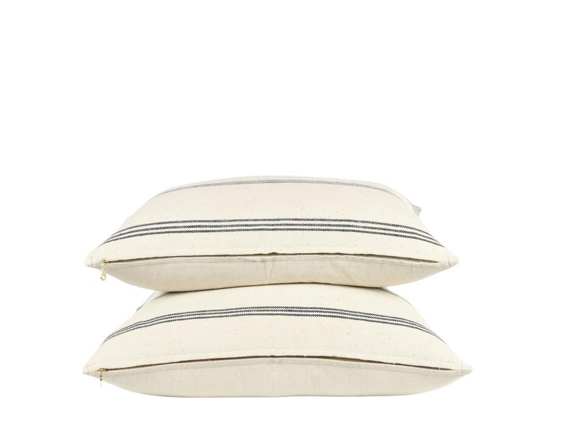 May include: Two white throw pillows with black stripes. The pillows are stacked on top of each other.