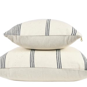 May include: Two white throw pillows with black stripes. The pillows are stacked on top of each other.