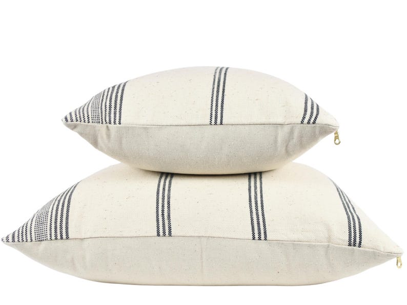 May include: Two white throw pillows with black stripes. The pillows are stacked on top of each other.