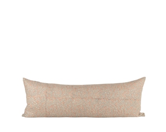 Puede incluir: Un cojín decorativo largo y rectangular con un fondo beige y un patrón repetido de pequeños elementos florales rojos y azules. El cojín está diseñado para una cama o un sofá.