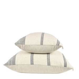 May include: Two white throw pillows with black stripes. The pillows are stacked on top of each other.