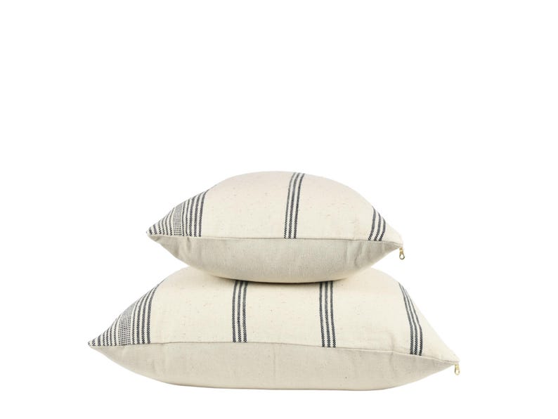 May include: Two white throw pillows with black stripes. The pillows are stacked on top of each other.