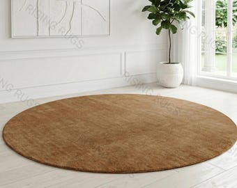 Puede incluir: Una alfombra circular grande de color marrón claro cálido con una textura de pelo corto y uniforme. La alfombra está colocada sobre un suelo claro, presentando un borde simple y limpio con una apariencia de superficie monocromática.