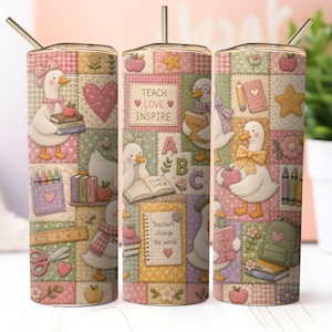 Op de afbeelding: Een cilindrische beker met een metalen rietje met een patchworkontwerp van witte eenden, appels, boeken, kleurpotloden en schoolspullen. De tekst luidt TEACH LOVE INSPIRE en Teachers change the world. Het patroon bevat hartjes, sterren en bloemen.