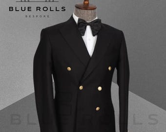 Peut inclure: Une veste de costume noire à double boutonnage avec des boutons dorés. La veste est sur un mannequin et porte un nœud papillon.