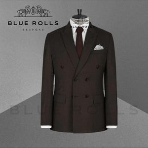 May include: A dark brown double-breasted suit with a white dress shirt, a brown tie, and a white pocket square. The suit is displayed on a mannequin. The logo "BLUE ROLLS BESPOKE" is visible in the upper left corner.