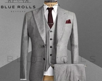 Può includere: Un abito grigio a tre pezzi con cravatta e fazzoletto da taschino bordeaux. La giacca del vestito ha una chiusura con un bottone e un revers a punta. Il gilet ha una chiusura con cinque bottoni. I pantaloni hanno un davanti piatto e una zip. L'abito è realizzato da Blue Rolls Bespoke.