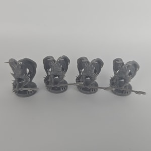 Pode incluir: Quatro miniaturas de dragões cinzentos com asas detalhadas e uma base em forma de lança. Os dragões estão em fila, cada um com uma pose única, provavelmente para jogos de tabuleiro ou colecionismo de modelos.