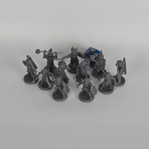 May include: A collection of eleven unpainted gray plastic miniature fantasy figures in various combat poses, each standing on a circular base. One blue twenty-sided die is positioned among the figures, which are armed with swords, shields, and staves.