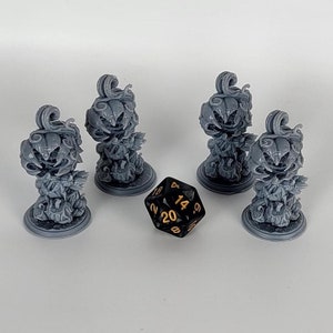 May include: Five gray, 3D-printed miniature figurines of jack-o'-lanterns with a 20-sided die. The jack-o'-lanterns have a spooky, smiling face and are surrounded by a smoky, flame-like design. The die is black with white numbers.