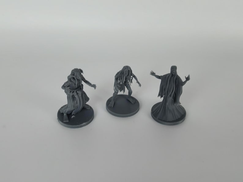 May include: Three gray 3D printed miniature figures of ghostly creatures. The figures are standing on round bases.