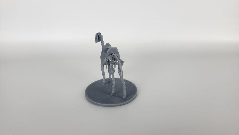 May include: A gray 3D printed miniature of a skeletal horse, standing on a round base.