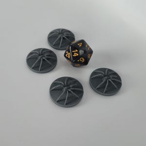May include: Five gray plastic spider web tokens and a black d20 dice with gold numbers. The dice shows a 14.