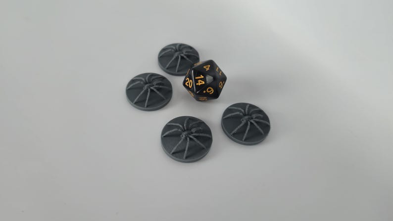 May include: Five gray plastic spider web tokens and a black d20 dice with gold numbers. The dice shows a 14.