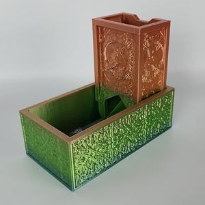 Puede incluir: Una torre de dados impresa en 3D con un acabado degradado verde y marrón. La torre tiene un diseño decorativo y una bandeja separada para atrapar los dados.