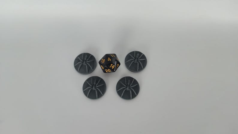 May include: Five gray plastic spider tokens and a black twenty-sided die with gold numbers.