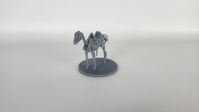 May include: A gray plastic miniature of a horse skeleton with a saddle on its back. The skeleton is standing on a round gray base.