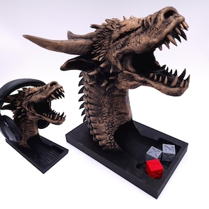 May include: A detailed dragon head sculpture in brown and black, with an open mouth and sharp teeth. One dragon head holds a pair of black headphones. The base of the larger dragon head has a compartment with three dice.