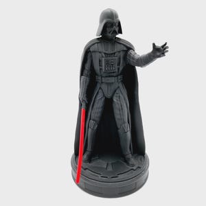Könnte beinhalten: Eine schwarze Darth Vader Actionfigur mit einem roten Lichtschwert. Die Figur steht auf einem schwarzen Sockel mit einem Star Wars Logo.