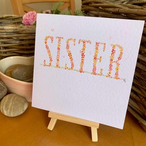 パーソナライズされた、オーダーメイドの、花で作られた繊細な「SISTER」という単語の手作り水彩カード。さまざまな個人的なメッセージに適しています。