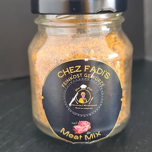 May include: A glass jar with a black lid filled with brown spice blend. The label reads "Chez Fadis Feinkost Gewürze" with a chef illustration and the text "Meat Mix".
