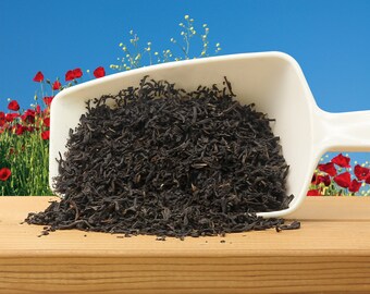 May include: A white scoop filled with loose leaf black tea. The tea is spilling out of the scoop onto a wooden surface.