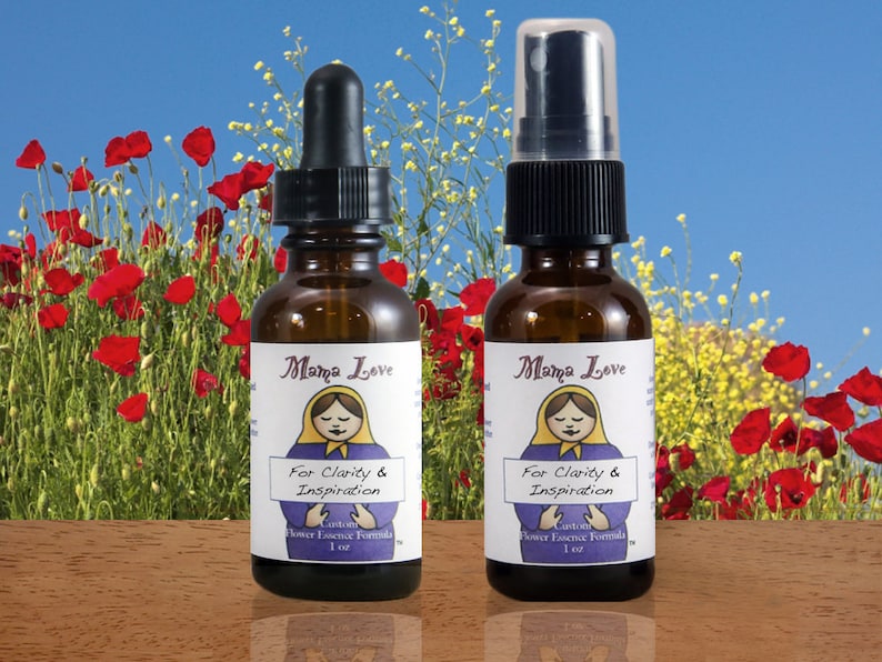 Op de afbeelding: Twee bruine glazen flessen met Mama Love bloemenessence. E&eacute;n heeft een druppelaar, de andere een sproeikop. Elke fles heeft een etiket met een Matroesjka-pop illustratie en de tekst "For Clarity & Inspiration". De achtergrond toont rode klaprozen en gele bloemen.