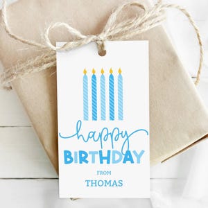 May include: A white birthday gift tag with blue candles and the words "happy BIRTHDAY" in blue script. The tag also says "FROM THOMAS". The tag is tied to a wrapped gift with twine.