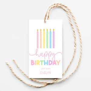 Pode incluir: Uma etiqueta de presente branca com um arco-&iacute;ris de velas e o texto "feliz anivers&aacute;rio" em letras rosa e azuis. O texto "com amor de Evelyn" est&aacute; impresso abaixo da sauda&ccedil;&atilde;o de anivers&aacute;rio.