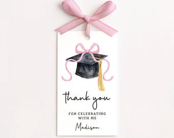Op de afbeelding: Een wit afstudeerbedankje met een roze lint. Het label toont een aquarel illustratie van een afstudeerhoed met een gouden kwast en roze lint accenten. De tekst luidt "bedankt voor het vieren met mij" en de naam "Madison".