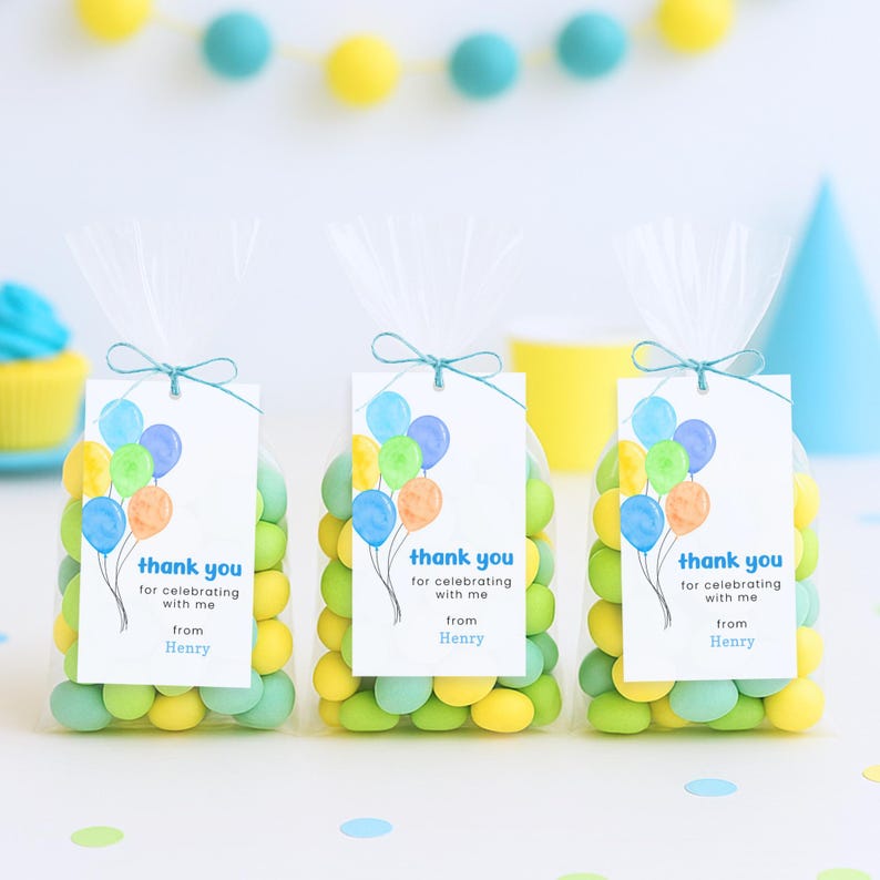 Puede incluir: Tres bolsas transparentes de celof&aacute;n llenas de caramelos coloridos, cada una atada con una cinta verde azulado. Adjuntas hay etiquetas con ilustraciones de globos y el texto "thank you for celebrating with me from Henry."