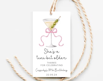 Può includere: Un'etichetta regalo bianca con un'illustrazione ad acquerello di un bicchiere da martini con un nastro rosa e olive. Il testo recita "She's a  tini bit older" e "Thanks for celebrating Cassidy's 28th Birthday 22.06.24".