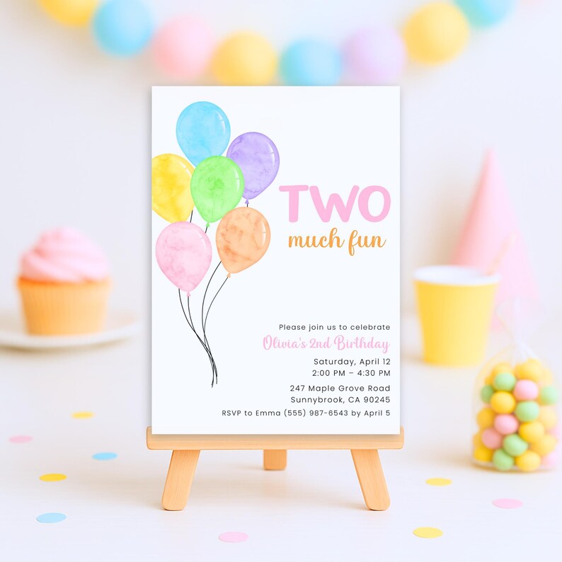 May include: A white invitation card on a small wooden easel, featuring watercolor balloons in various colors. The text reads "TWO much fun" and invites guests to Olivia's 2nd birthday party. Additional details include the date, time, and location.