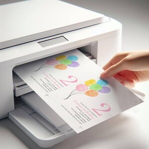 May include: A white printer is shown printing a birthday invitation. The invitation features watercolor balloons in various colors and the number "2" in pink. A hand is pulling the printed invitation from the printer.