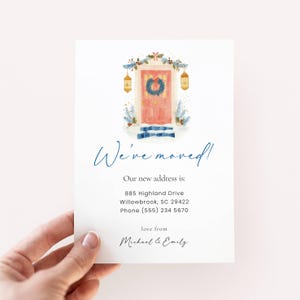May include: A white card with the text "We've moved!" in a handwritten font. The card features a watercolour illustration of a pink door decorated with a wreath and winter foliage. The new address and contact information are also included.