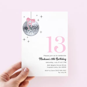 Op de afbeelding: Een witte rechthoekige uitnodigingskaart met een zilveren discobal met een roze strik, zwarte steraccenten en het grote roze getal 13. De tekst luidt: Please join us to celebrate Madison's 13th Birthday, Saturday, July 31 at 2 PM, 842 Maple Grove Drive, Franklin Hills, OH 43016, RSVP to Sara (512) 555 0147 by July 25.