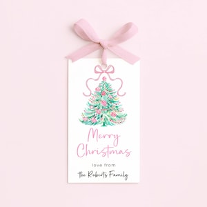 May include: A white gift tag with a watercolor Christmas tree design, pink accents, and a pink ribbon. The tag reads "Merry Christmas" and "love from the Roberts Family".