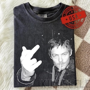 Könnte beinhalten: Schwarzes T-Shirt mit einem Schwarz-Weiß-Bild einer Person mit Zigarette und Handgeste. Das Shirt hat einen Used-Look und der Text "KIMSLU" ist sichtbar.