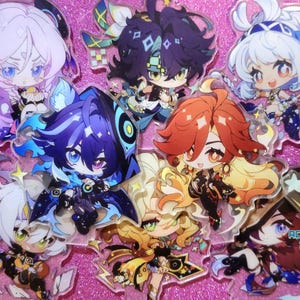 May include: A collection of colorful anime character acrylic charms. The charms feature characters with different hair colors, outfits, and expressions. The charms are on a pink background.