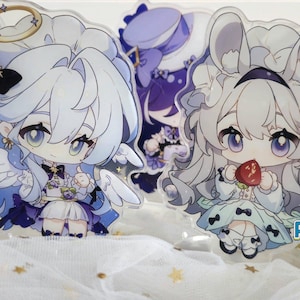 May include: Two anime-style acrylic character stands. The character on the left is wearing a white dress with blue and purple accents, a halo, and angel wings. The character on the right is wearing a white dress with blue and green accents, a white bunny ear headband, and a red apple in her hand. The text "ACGCrafts" is visible in the bottom right corner of the image.